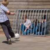 A schoolyard bully kicks a soccer ball at some younger children