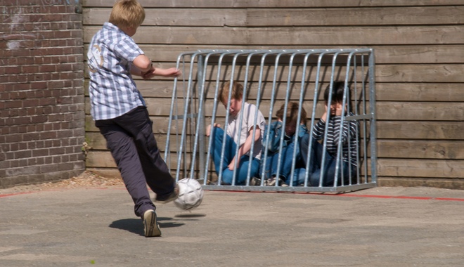 A schoolyard bully kicks a soccer ball at some younger children